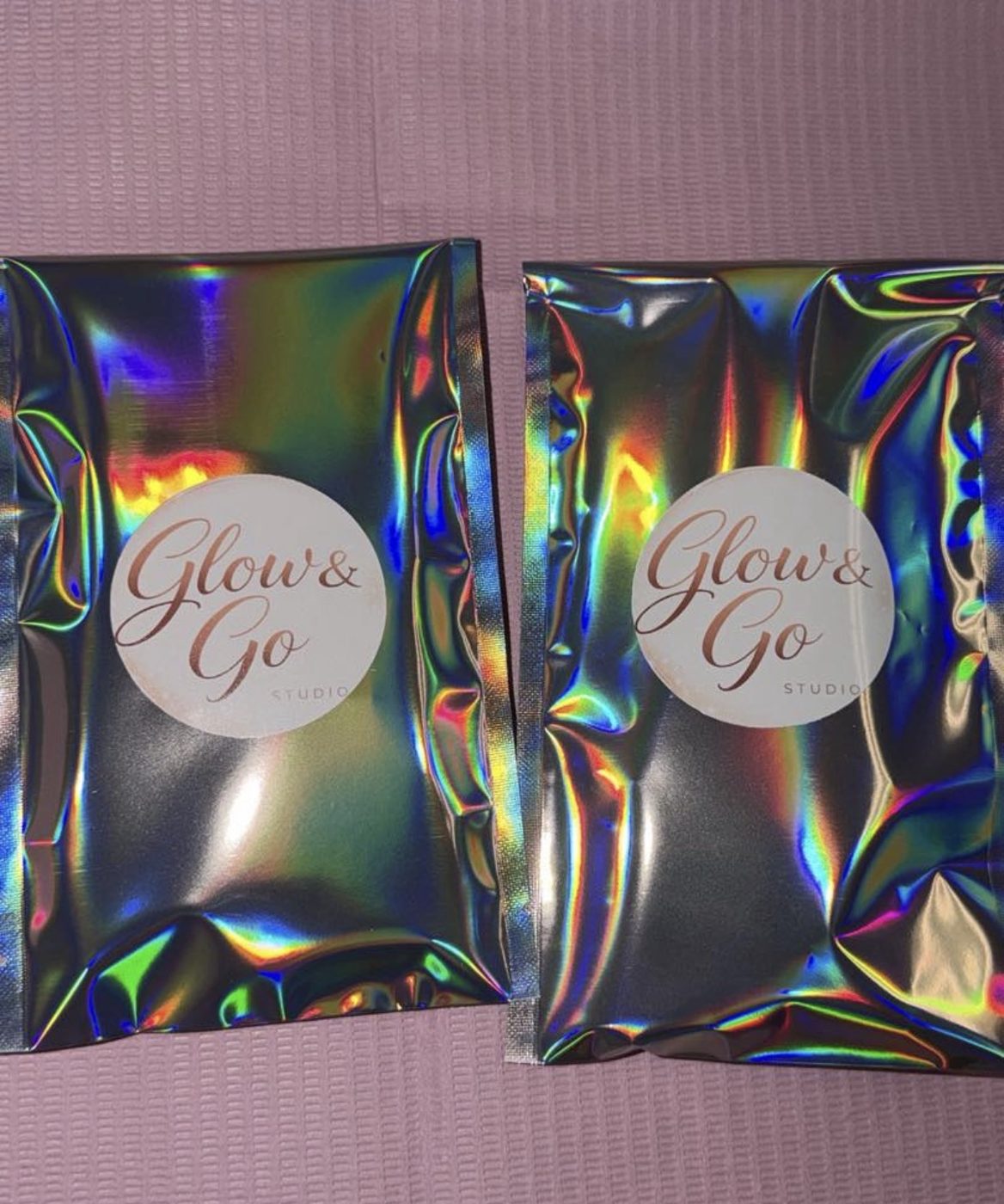 Glow & Go Studio branded holographic mailer packets on a soft pink surface
