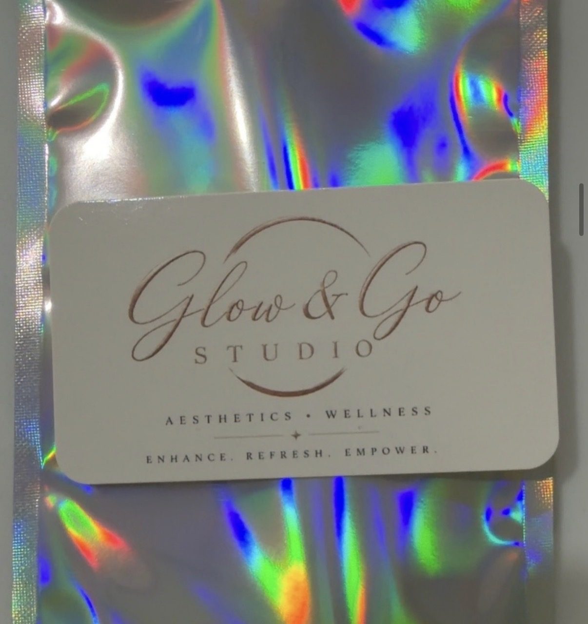 Glow & Go Studio business card resting on a holographic mailer packet
